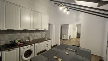 A modern kitchen with white cabinets, a built-in washing machine, and a dining area with a table set for four.
