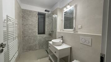Une salle de bain moderne avec un mur en pierre, un lavabo blanc, un miroir et des toilettes.