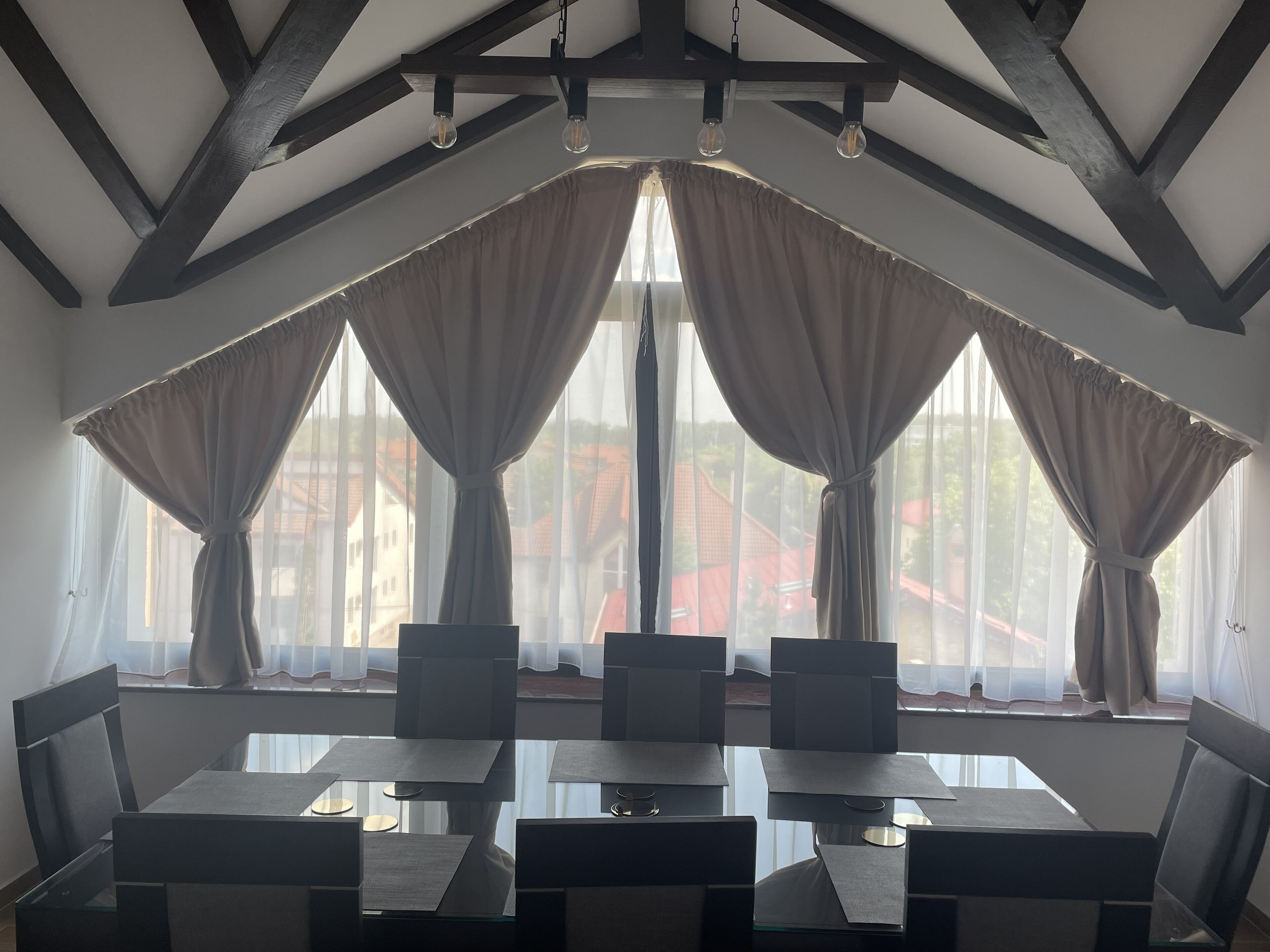 A dining area with a high ceiling, exposed beams, and large windows with curtains.