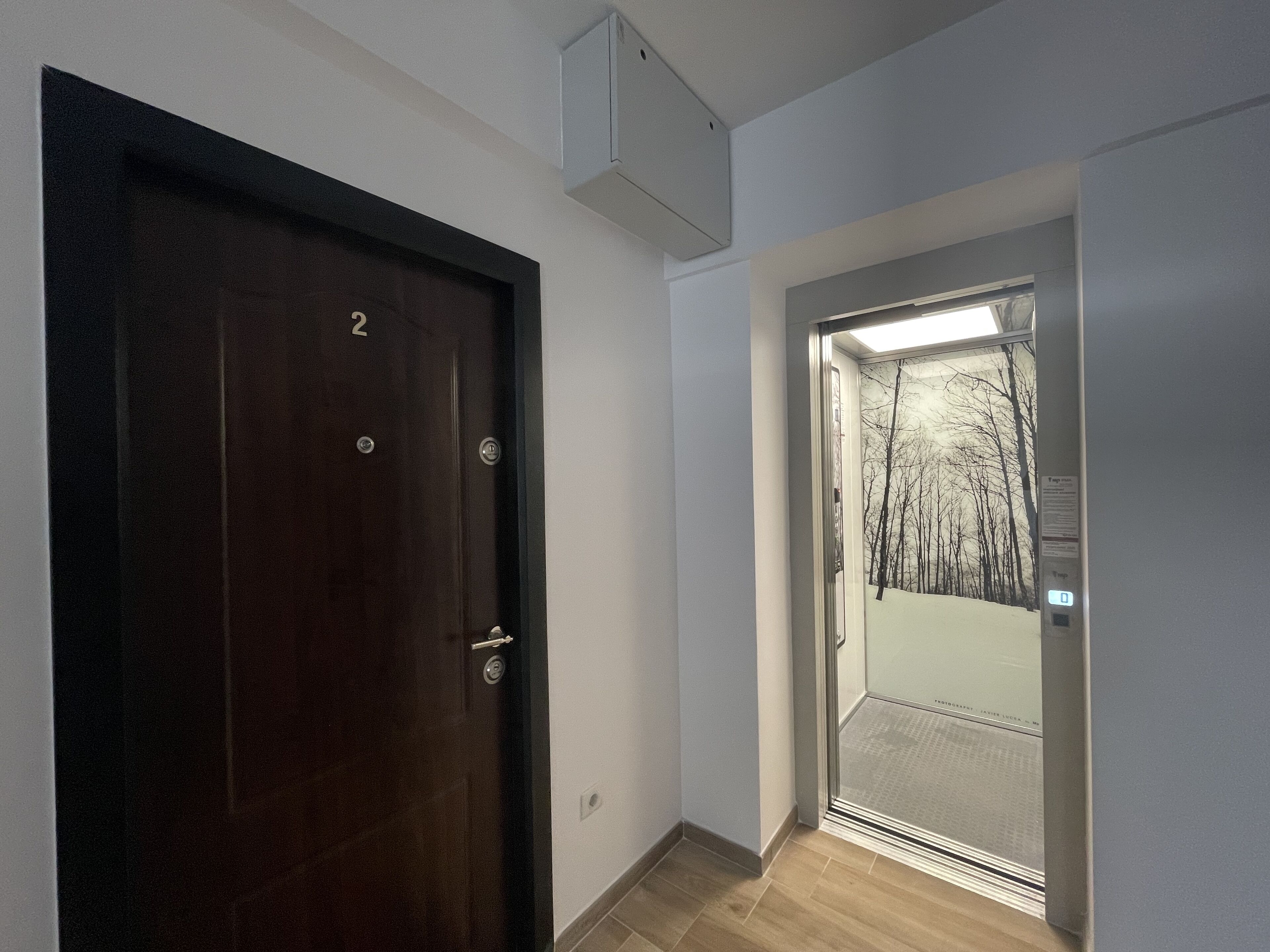 Un couloir avec une porte en bois portant le numéro « 2 » et une porte d’ascenseur en verre.