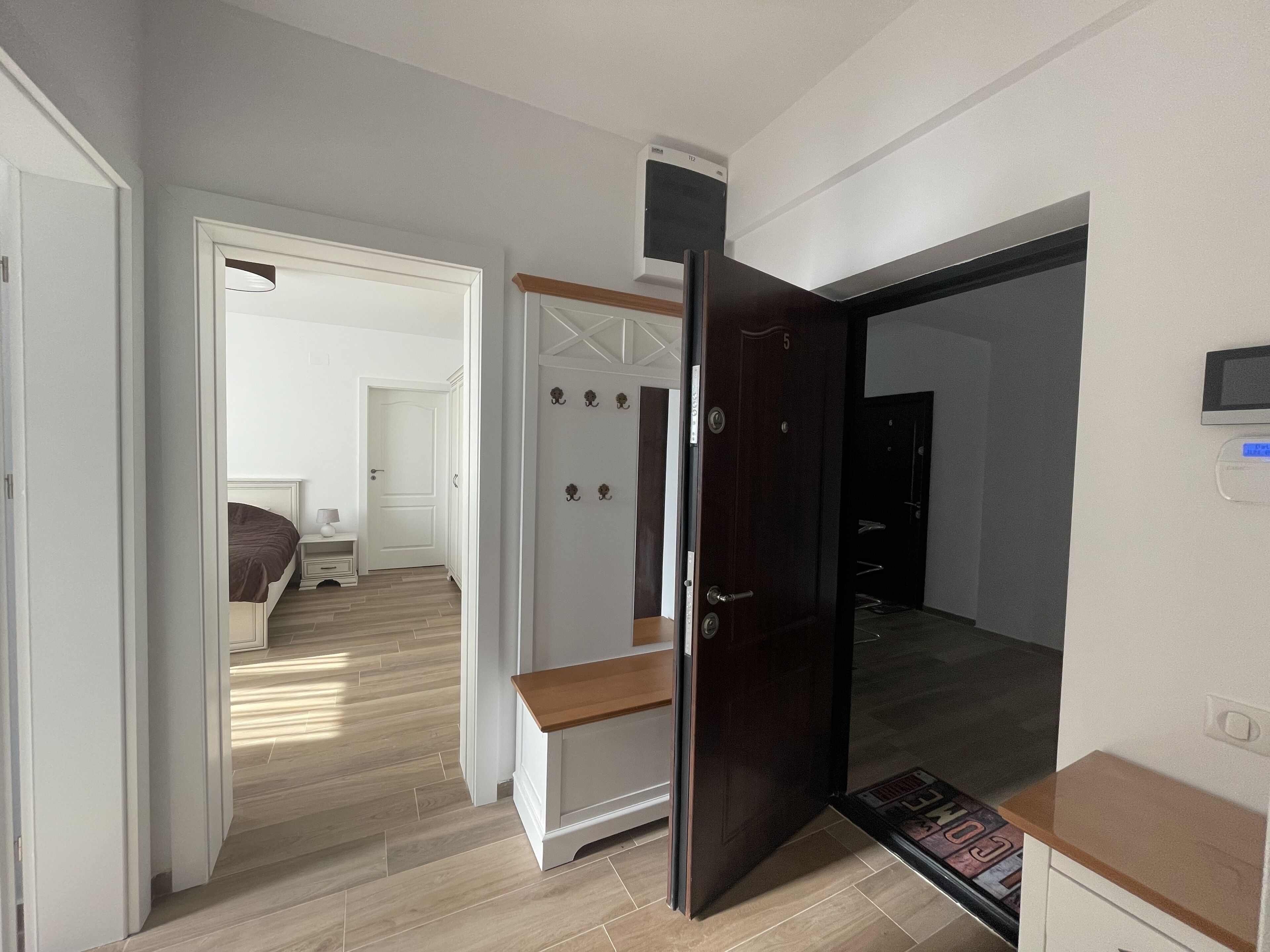 A hallway with a wooden bench, a white door, and a dark door leading to another room.