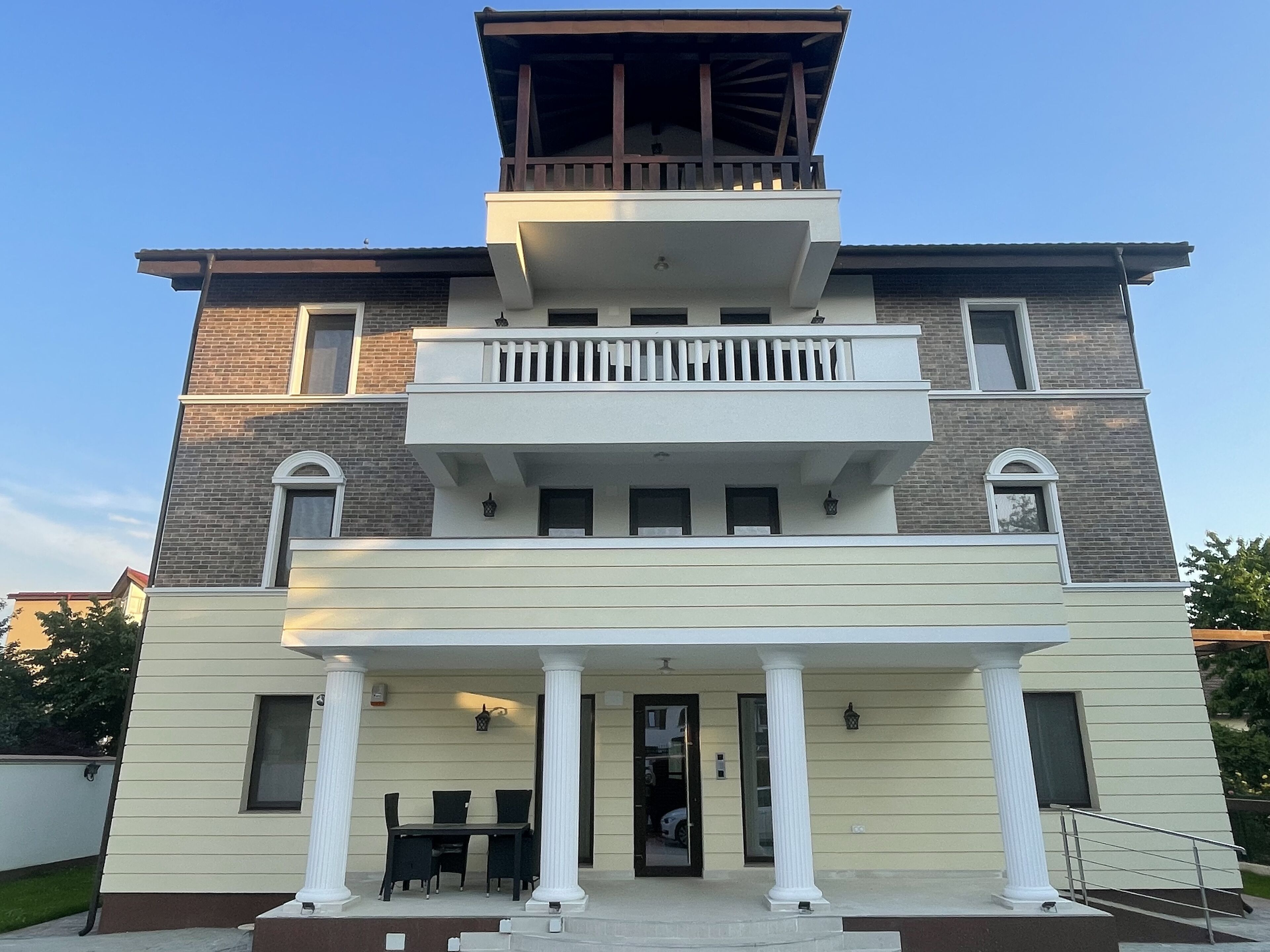 Un edificio a due piani con un balcone al piano superiore, un portico coperto al piano terra e un piccolo tavolo con sedie all'esterno.