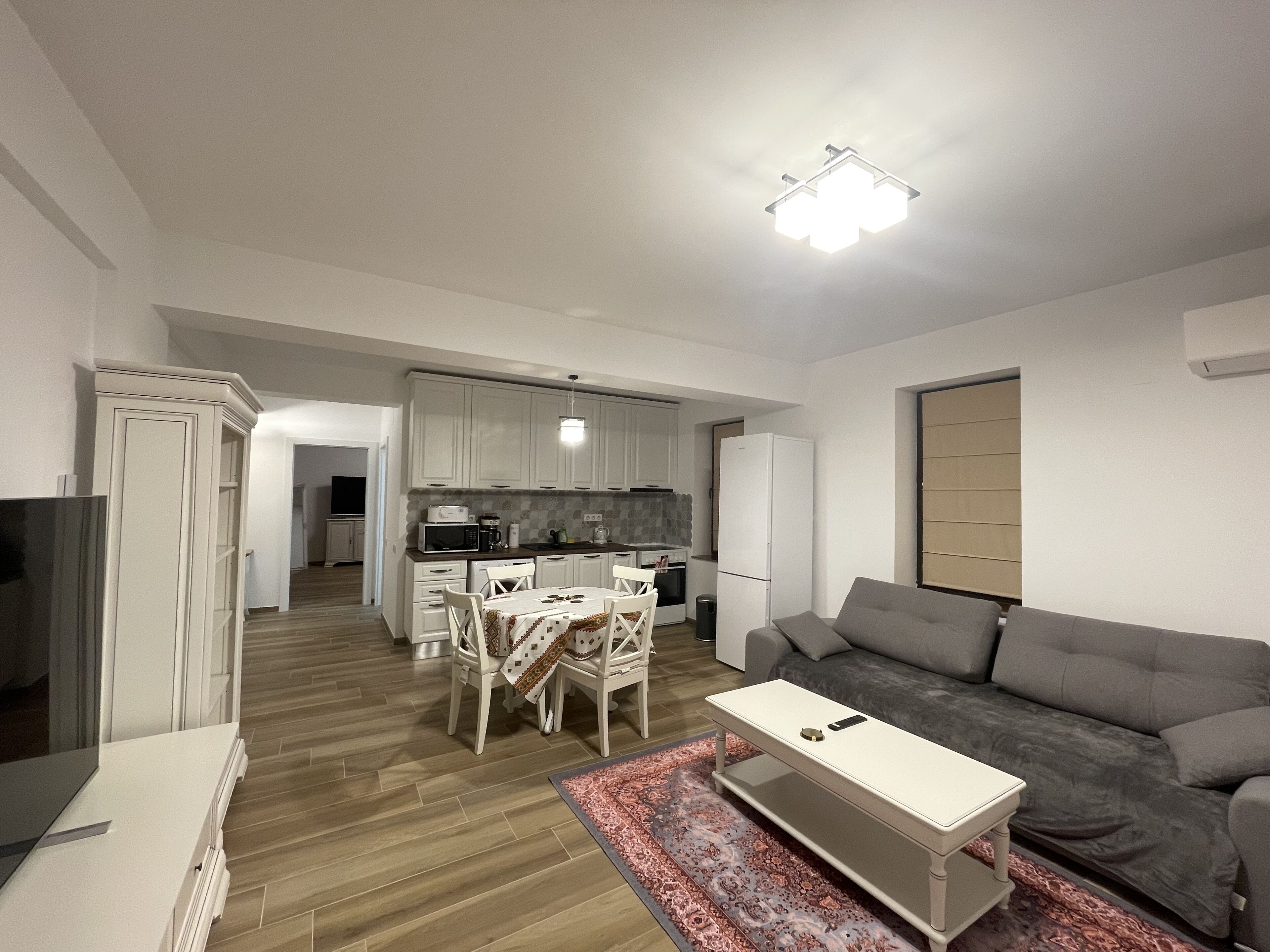 A modern living room with a grey sofa, a white coffee table, and a dining area with a table and chairs.
