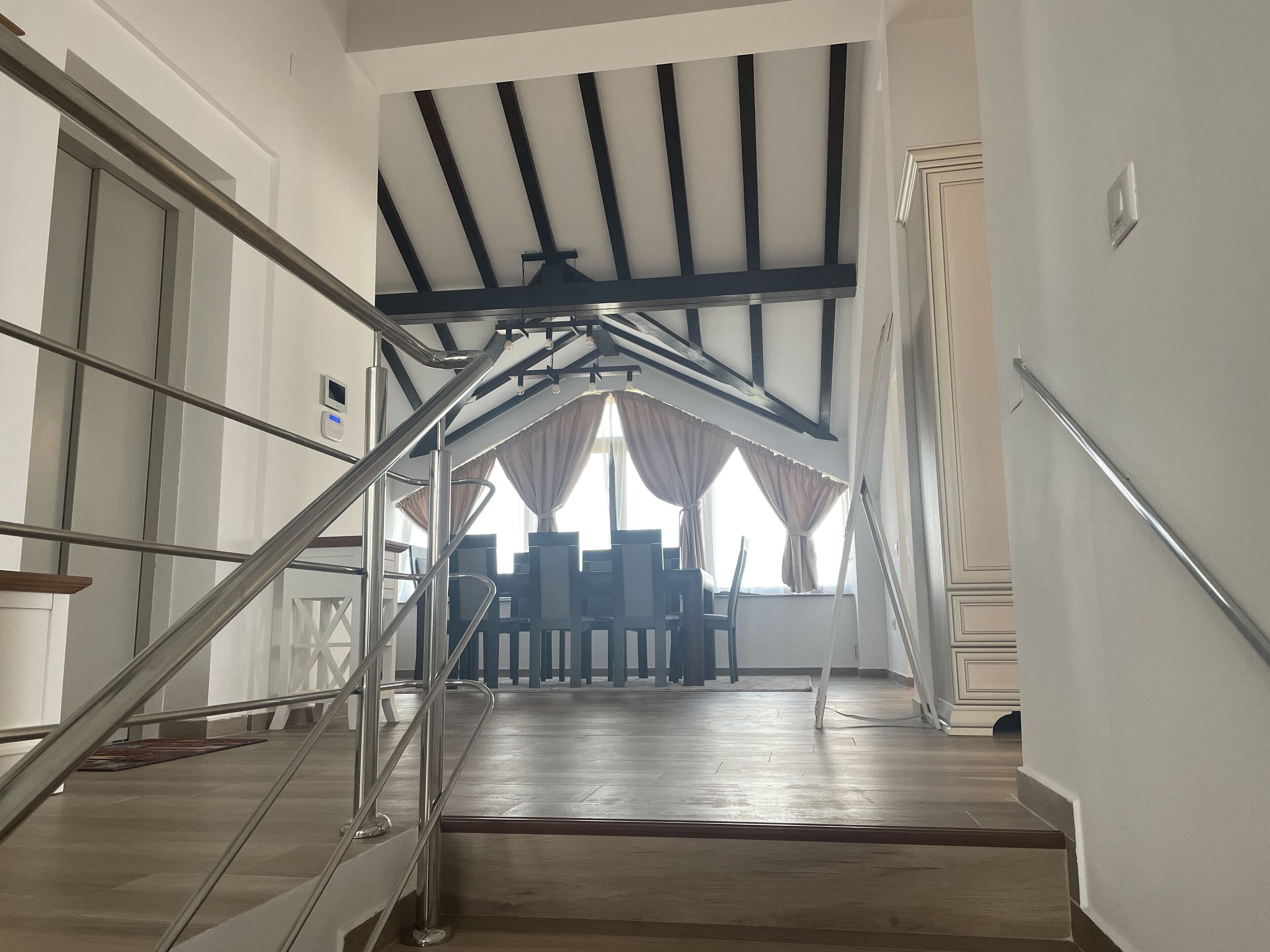 A staircase with metal railings leading to a room with a wooden floor and a view of a dining area.