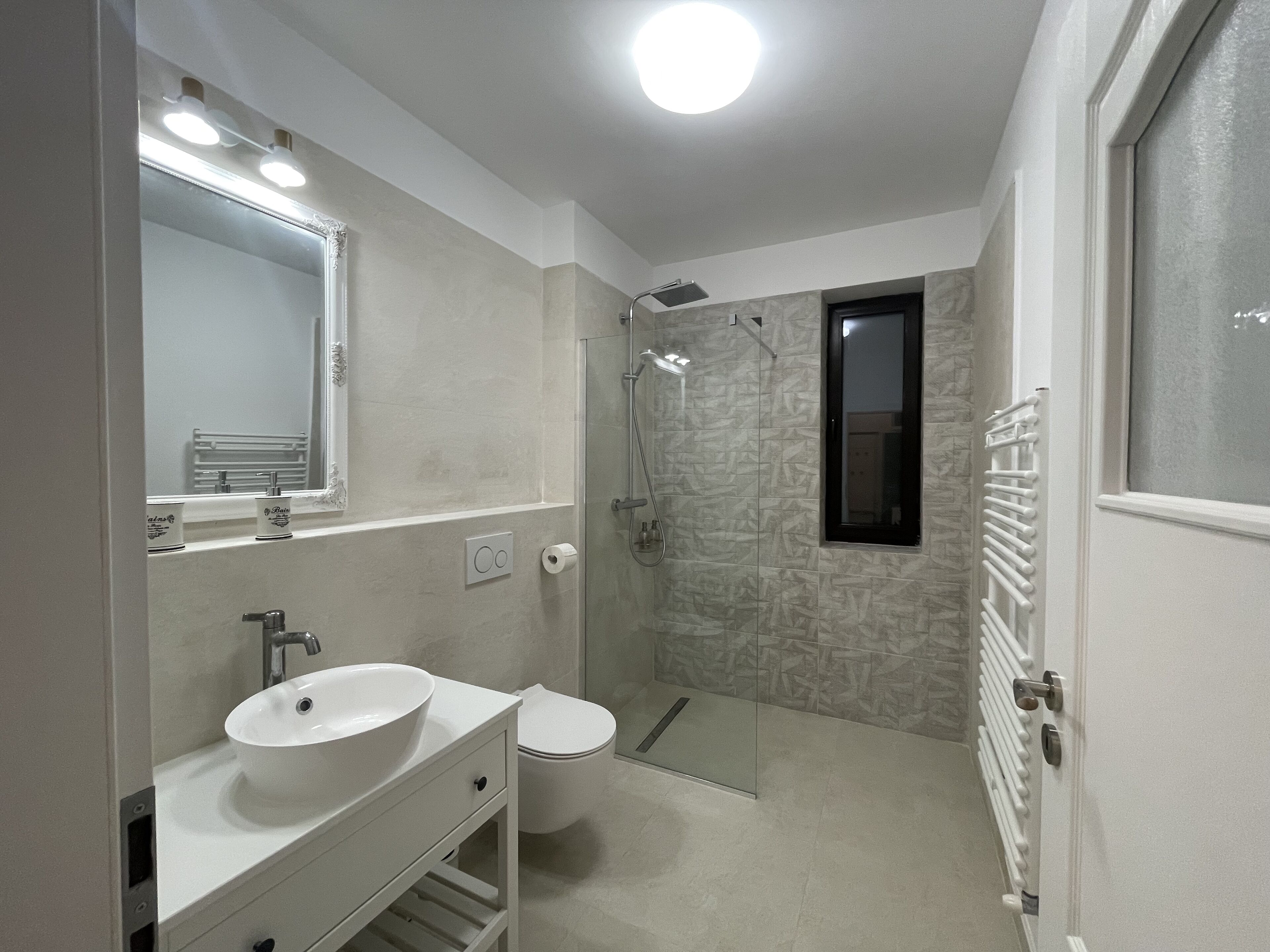 A modern bathroom with a large mirror, a sink, a toilet, and a shower.