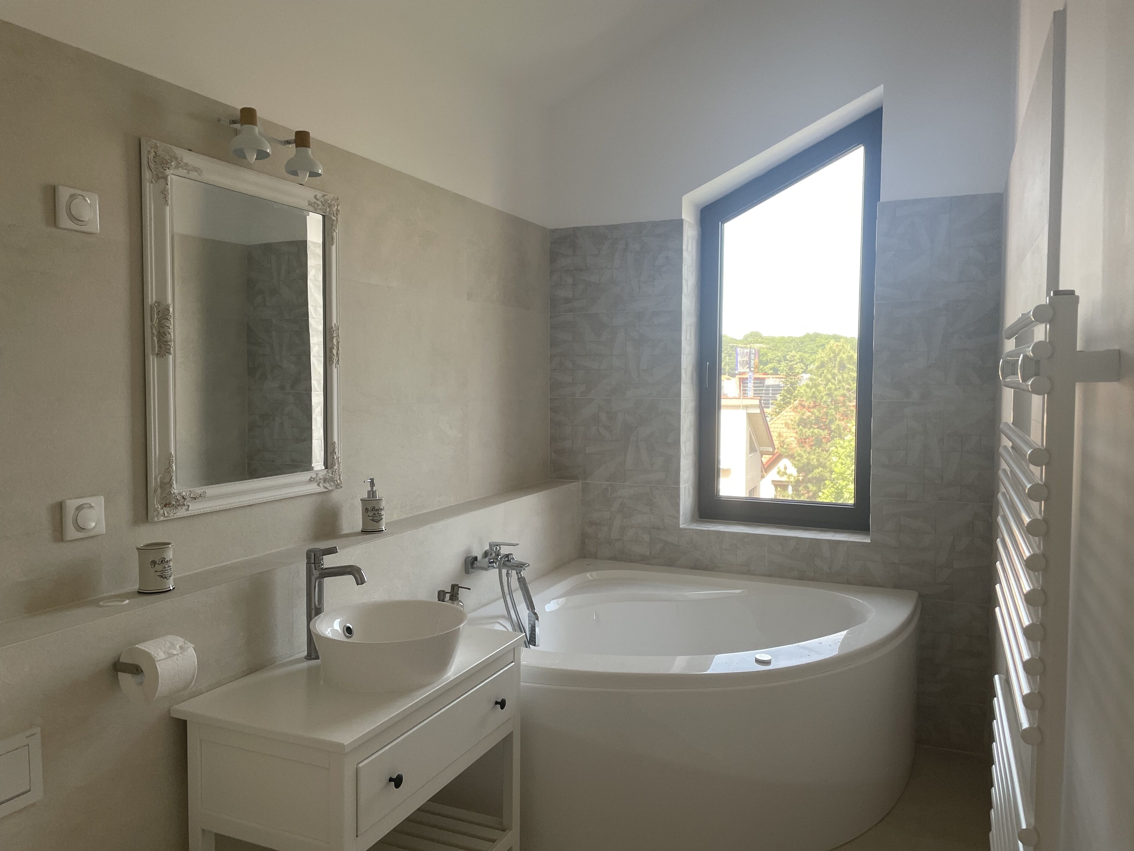 A modern bathroom with a freestanding bathtub, a large mirror, and a window providing a view of greenery outside.