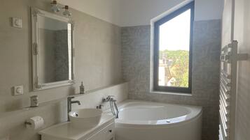 A modern bathroom with a freestanding bathtub, a large mirror, and a window providing a view of greenery outside.