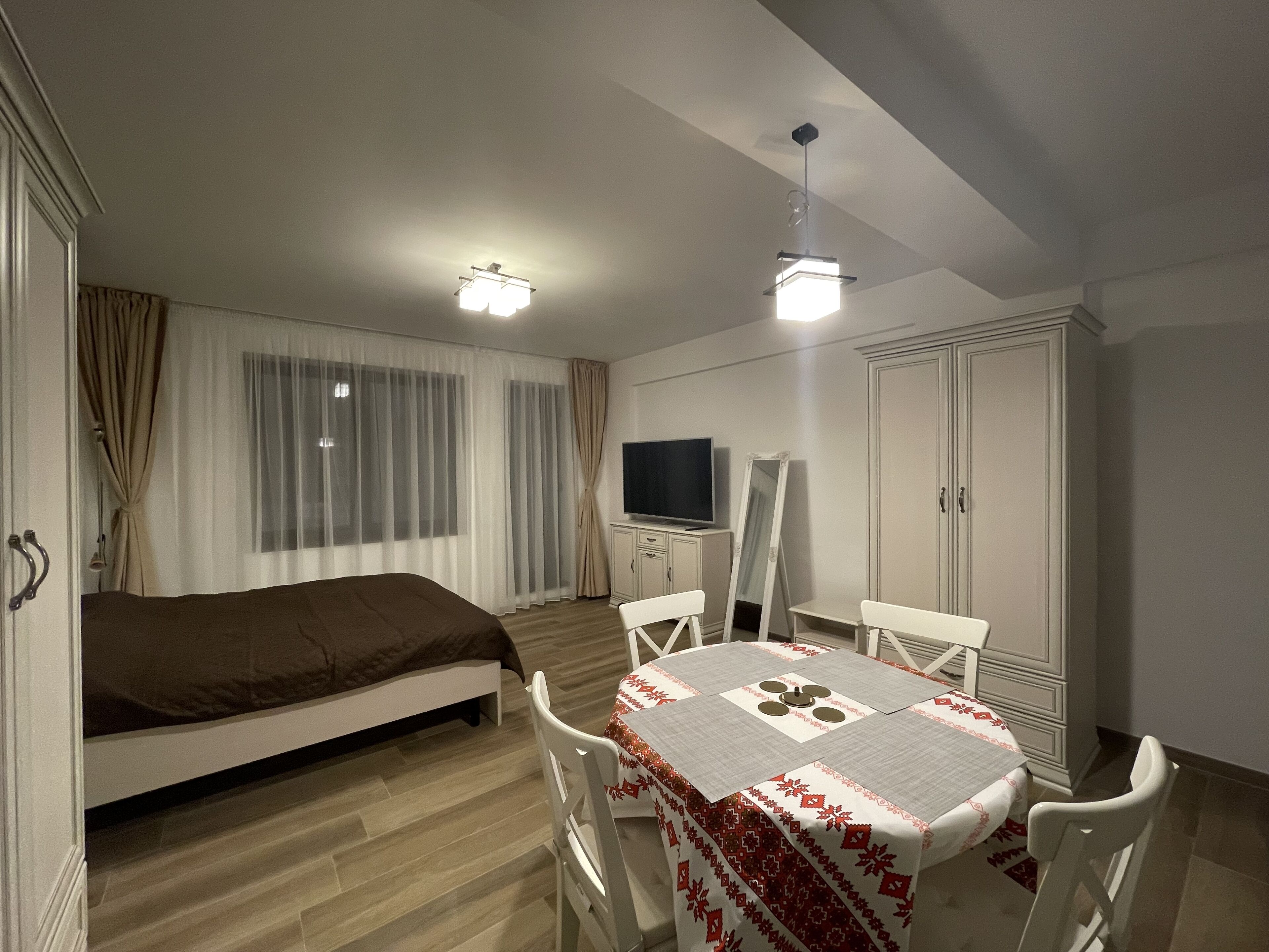 Een slaapkamer met een bed, een televisie, een garderobe en een eettafel met stoelen.