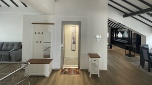 Un interior moderno con una escalera que conduce a una zona superior, un sofá gris y una mesa de comedor con sillas.