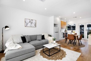 Una sala de estar moderna con un sofá gris, una mesa de centro blanca y un comedor con sillas de madera y una mesa.