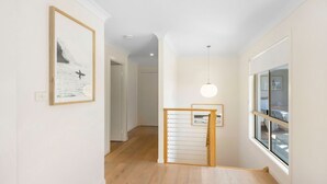 A hallway with wooden flooring, a staircase with a wooden railing, and a large window with a view of the outdoors.