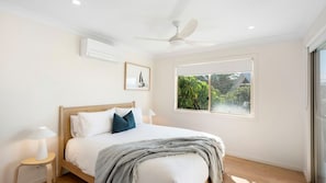 Un dormitorio con cama, ventilador de techo, ventana con vistas a la vegetación y un equipo de aire acondicionado.