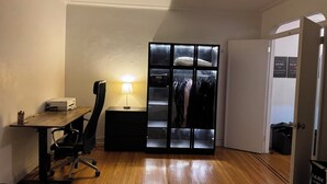 A compact room with a wooden desk, a chair, a lamp, and a wardrobe with a mirror. - Two Large Cozy Bedroom Condominium that is 20 mins train ride to Manhattan
 (Queens)