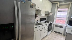 A kitchen with white cabinets, a stainless steel refrigerator, a gas stove, and a window with a view of the outside. - Two Large Cozy Bedroom Condominium that is 20 mins train ride to Manhattan
 (Queens)