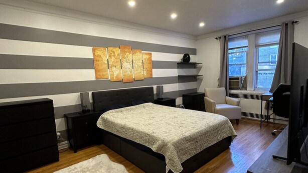 A modern bedroom with a large bed, a world map artwork, a white rug, and a window with curtains. - Two Large Cozy Bedroom Condominium that is 20 mins train ride to Manhattan
 (Queens)