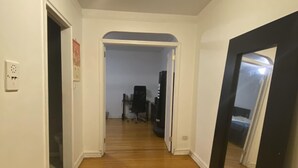 A hallway with wooden flooring, white walls, and a ceiling light. - Two Large Cozy Bedroom Condominium that is 20 mins train ride to Manhattan
 (Queens)