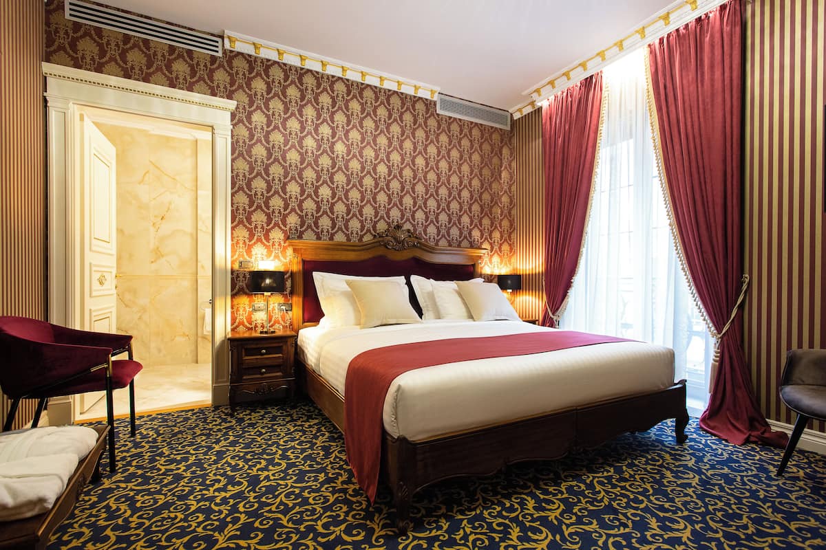 A hotel room with a large bed, a vanity with a mirror, a chair, and a door leading to a bathroom.