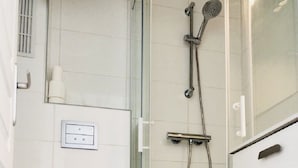 Bany amb dutxa de vidre, vàter i un moble amb calaixos.