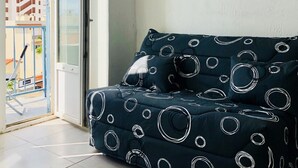 Un balcó amb un sofà blau fosc amb dibuixos circulars, una barana de metall i vista a edificis.