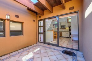 Un patio amplio con suelo de baldosas, una puerta corrediza de vidrio que da a una zona de cocina y un pequeño rincón con mobiliario de exterior.
