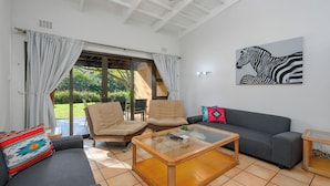 A living room with a sofa, two armchairs, a glass coffee table, and a zebra artwork on the wall. - San Lameer Villa 2018 (Southbroom)