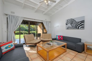 Ein Wohnzimmer mit einer Couch, zwei Sesseln, einem Glastisch und einem Zebrabild an der Wand.