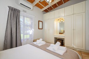 Un dormitorio con cama, espejo, armario y ventana con cortinas.