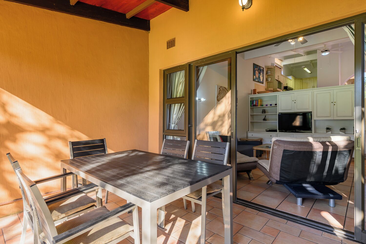 A dining area with a table and chairs, a sliding glass door leading to a kitchen, and a small seating area with a bench.