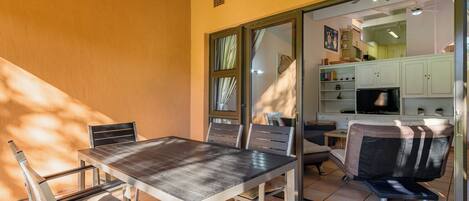 A dining area with a table and chairs, a sliding glass door leading to a kitchen, and a small seating area with a bench.