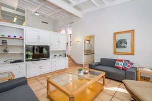 Una sala moderna con sofá, mesa de centro y televisor. Una escalera conduce a una cocina.