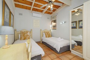 Un dormitorio con dos camas, ventilador de techo, aire acondicionado y un espejo.
