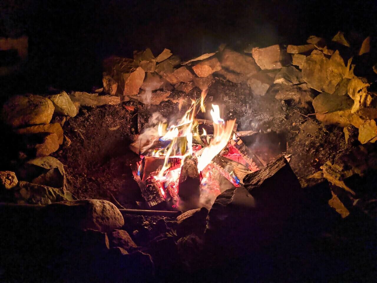 A campfire surrounded by rocks and logs.