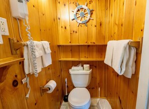 A wooden-paneled bathroom with a ship's wheel decoration, a toilet, and towels hanging on racks. - Isleview Cottage 5 - 2 min to Mount Desert Isle! (Trenton)