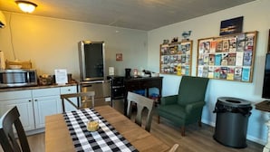 Una cucina compatta con elettrodomestici moderni, un tavolo da pranzo con tovaglia a quadri e una poltrona verde.