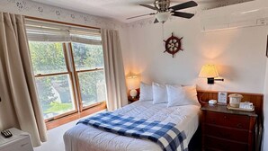 A neatly arranged bedroom with a bed, bedside lamps, a nightstand, a ceiling fan, and a window with curtains.