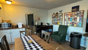 Una cocina compacta con electrodomésticos modernos, una mesa de comedor con mantel a cuadros y un sillón verde.
