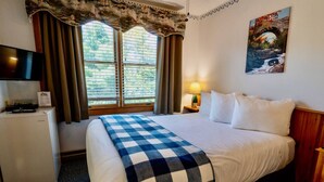 Una habitación de hotel con cama, televisión, escritorio y ventana con cortinas.