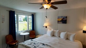 Une chambre d’hôtel équipée d’un lit, d’un bureau, d’une chaise, d’un ventilateur de plafond et d’une fenêtre avec des rideaux.
