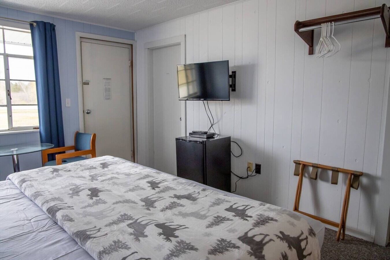 Una habitación de hotel con una cama, un escritorio, una silla, un televisor y un perchero.