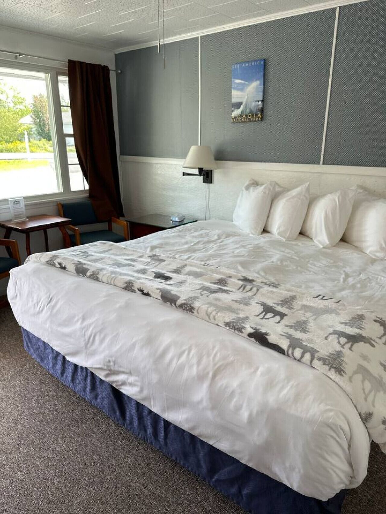 A hotel room with a large bed, a desk, a chair, and a window with curtains.