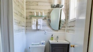 Un bagno compatto con toilette, lavandino e specchio. È presente un portasciugamani con asciugamani, un piccolo cestino e una finestra che offre luce naturale.