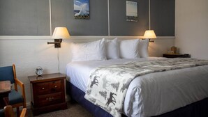 Un letto rifatto con cura, una coperta fantasia, due abat-jour, un comodino in legno con una sveglia e due poster alle pareti.