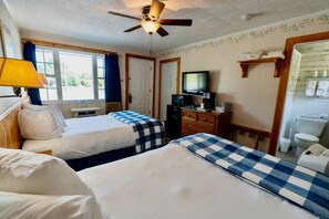 A hotel room with two beds, a ceiling fan, a television, a dresser, and a bathroom.