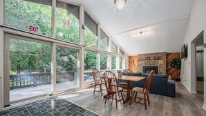 Una habitación amplia con ventanas grandes, un comedor con sillas de madera, un sofá azul y una chimenea.