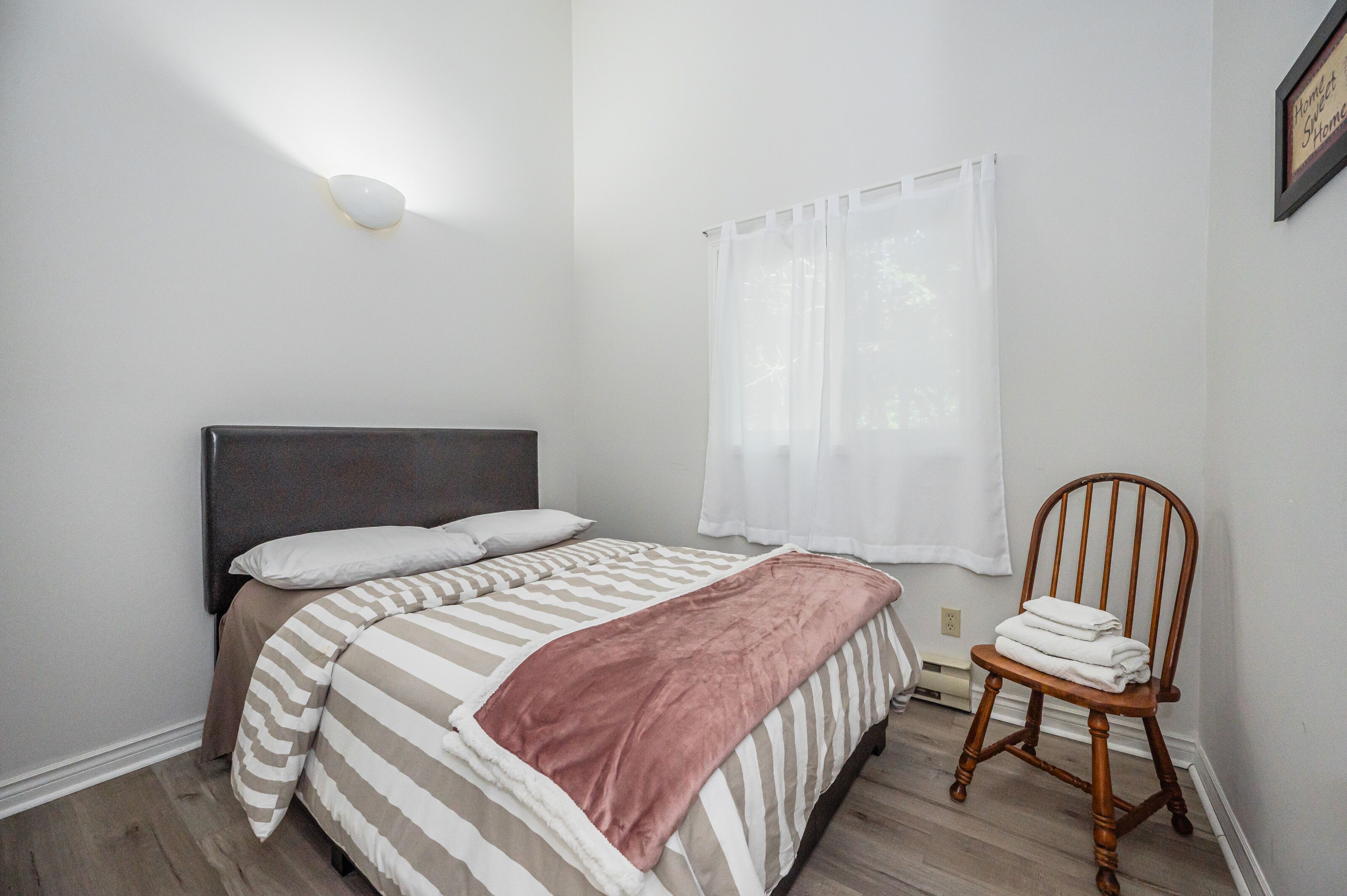 A bedroom with a bed, a chair, a wall-mounted light, and a window with curtains.
