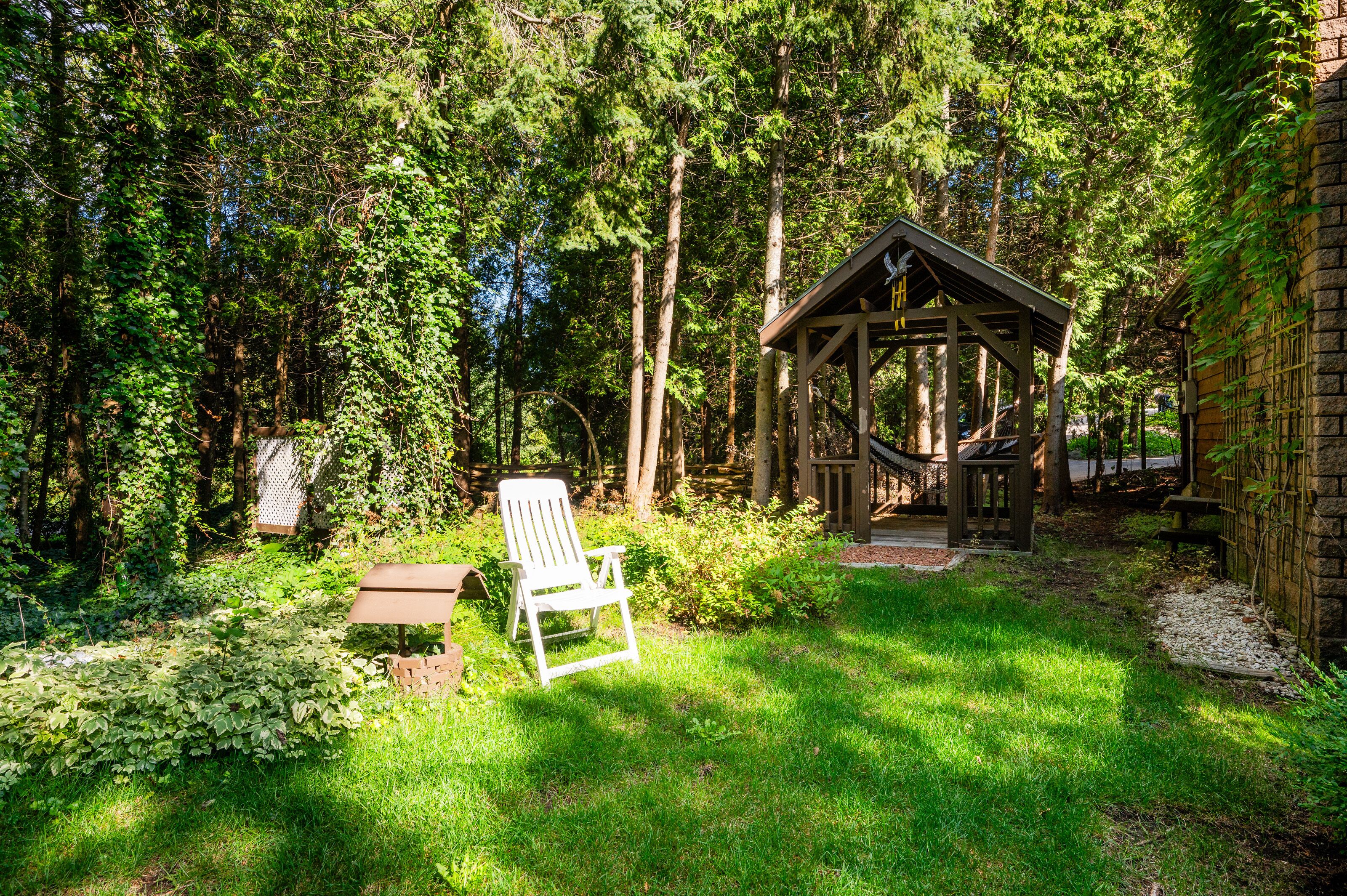 A wooden gazebo with a bench and a chair in a lush garden.