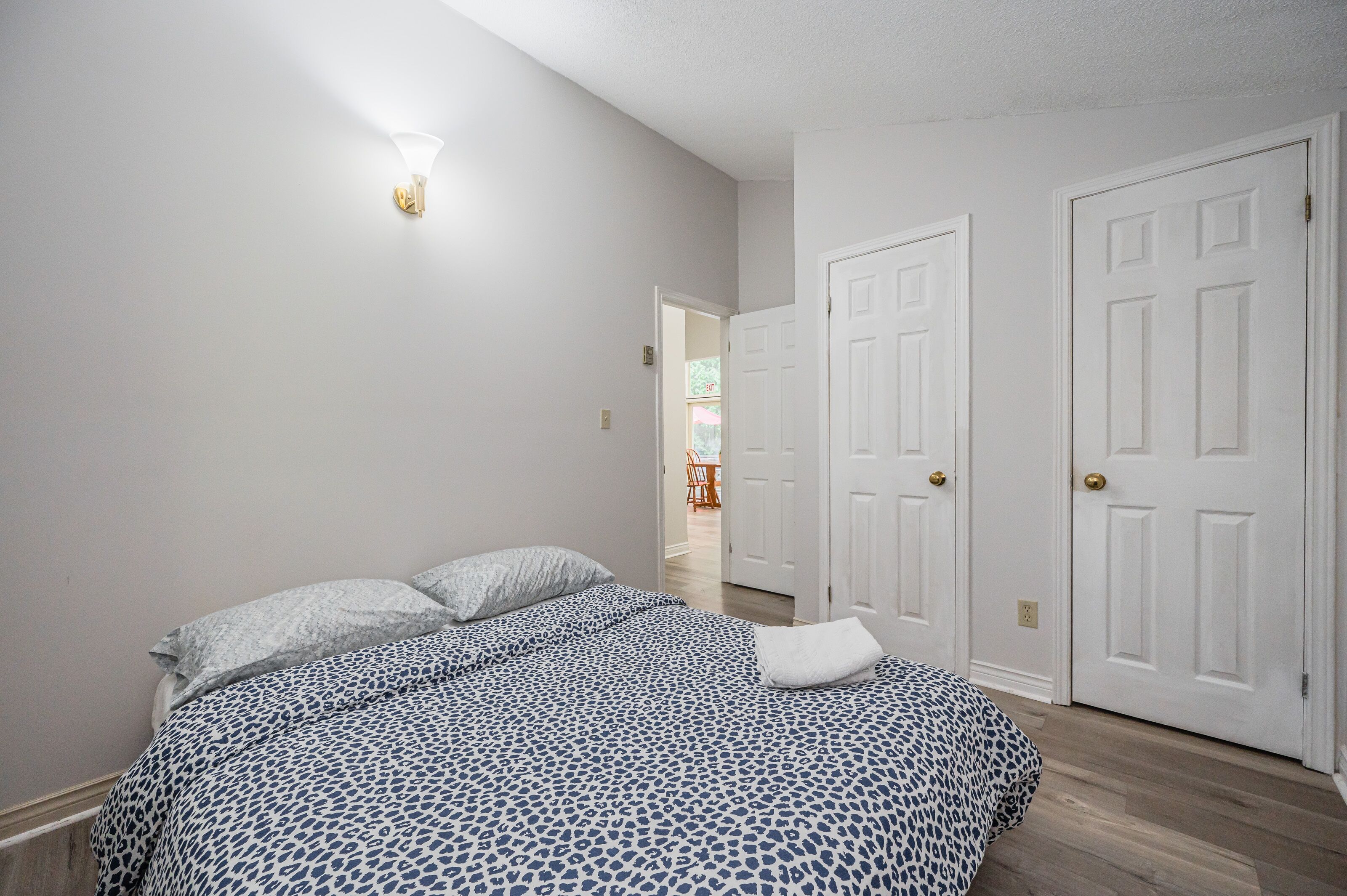A bedroom with a bed, two white doors, and a hallway leading to another room.