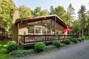 Un chalet avec une façade en pierre, de grandes fenêtres, une terrasse en bois et un parasol rouge.