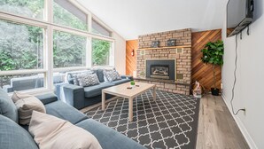 A modern living room with a fireplace, large windows, and a grey sofa.