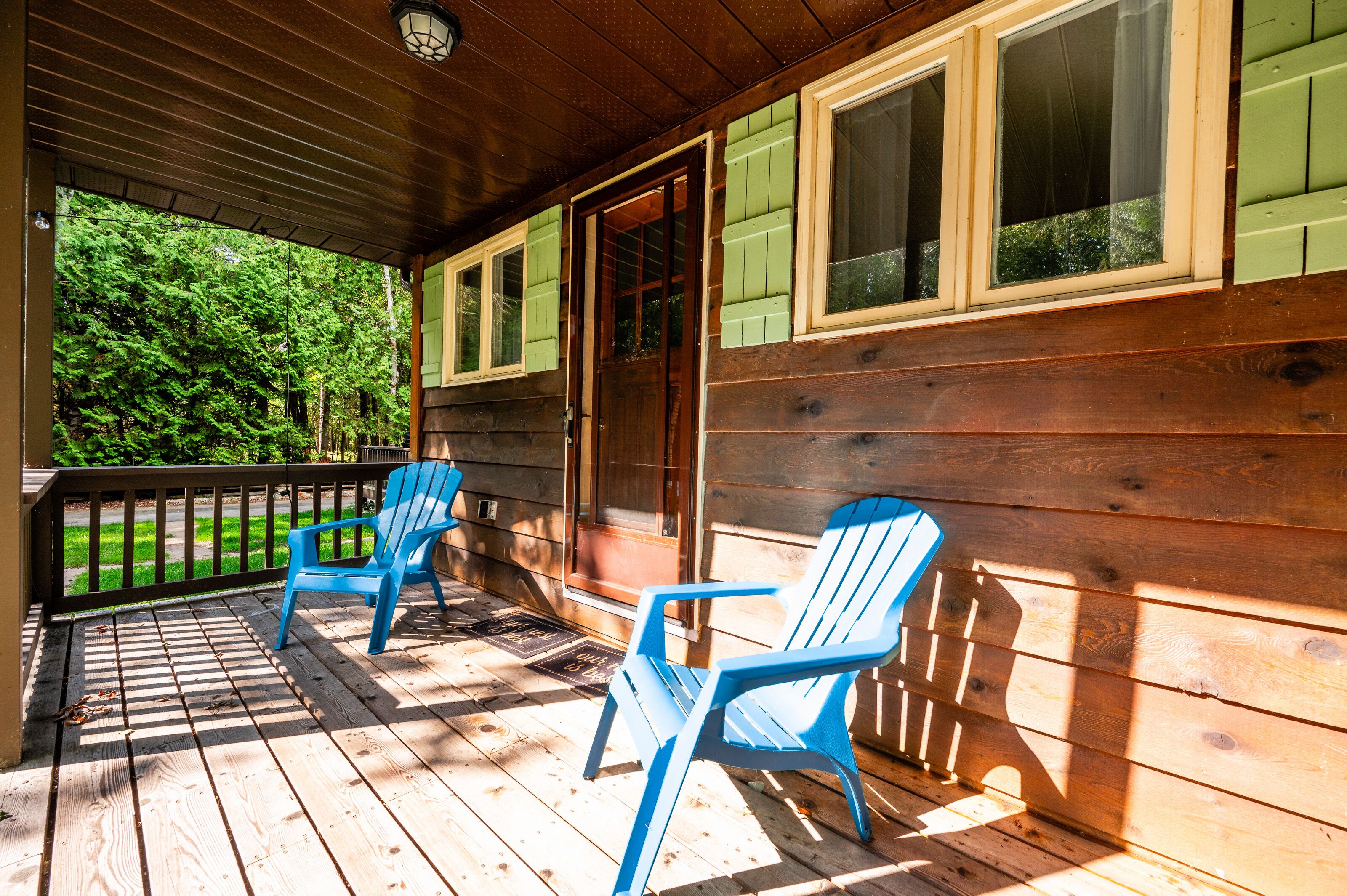 Un porche de madera con dos sillas Adirondack azules y una puerta de madera.